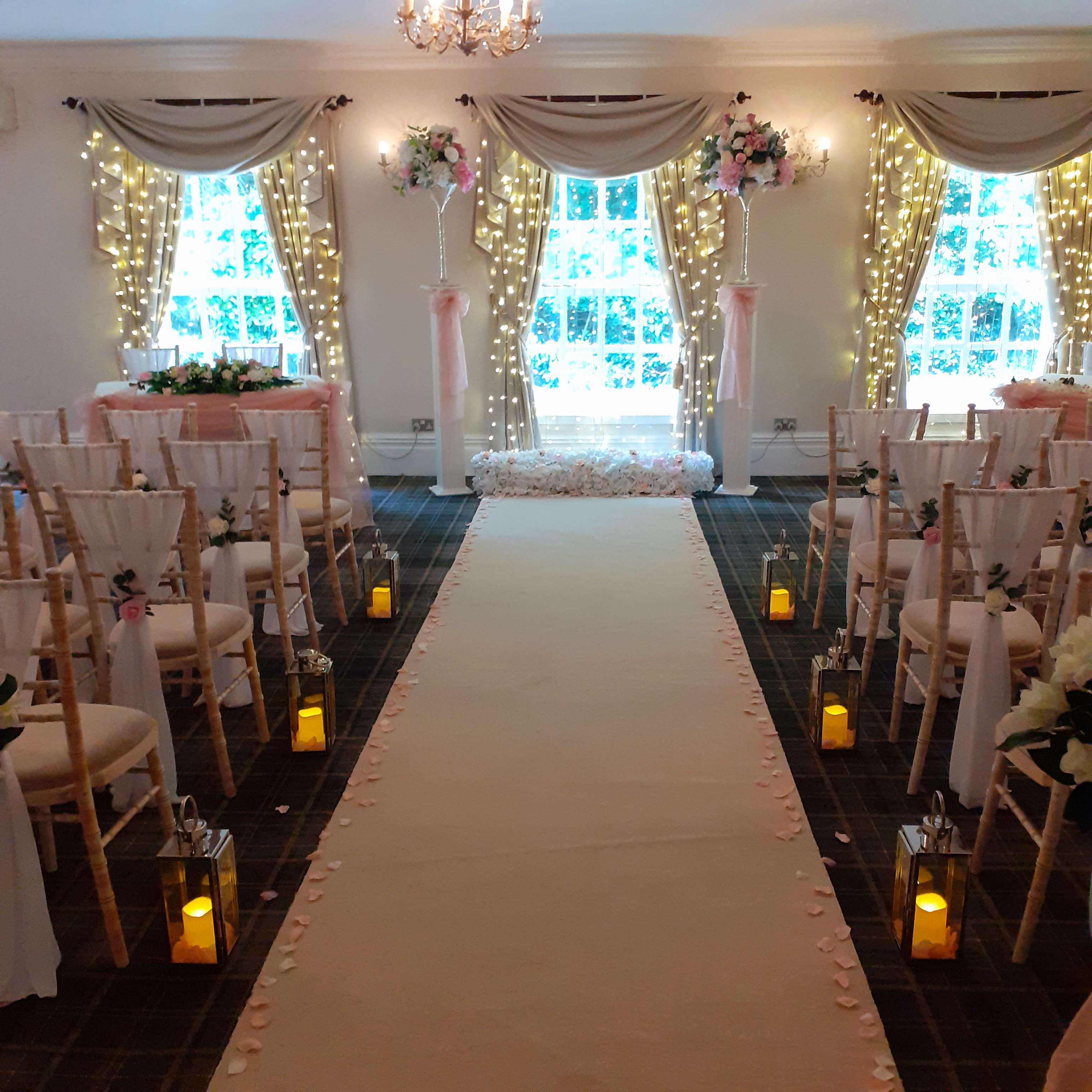 Wedding ceremony set up with aisle carpet lanterns flowers chairs with drapes